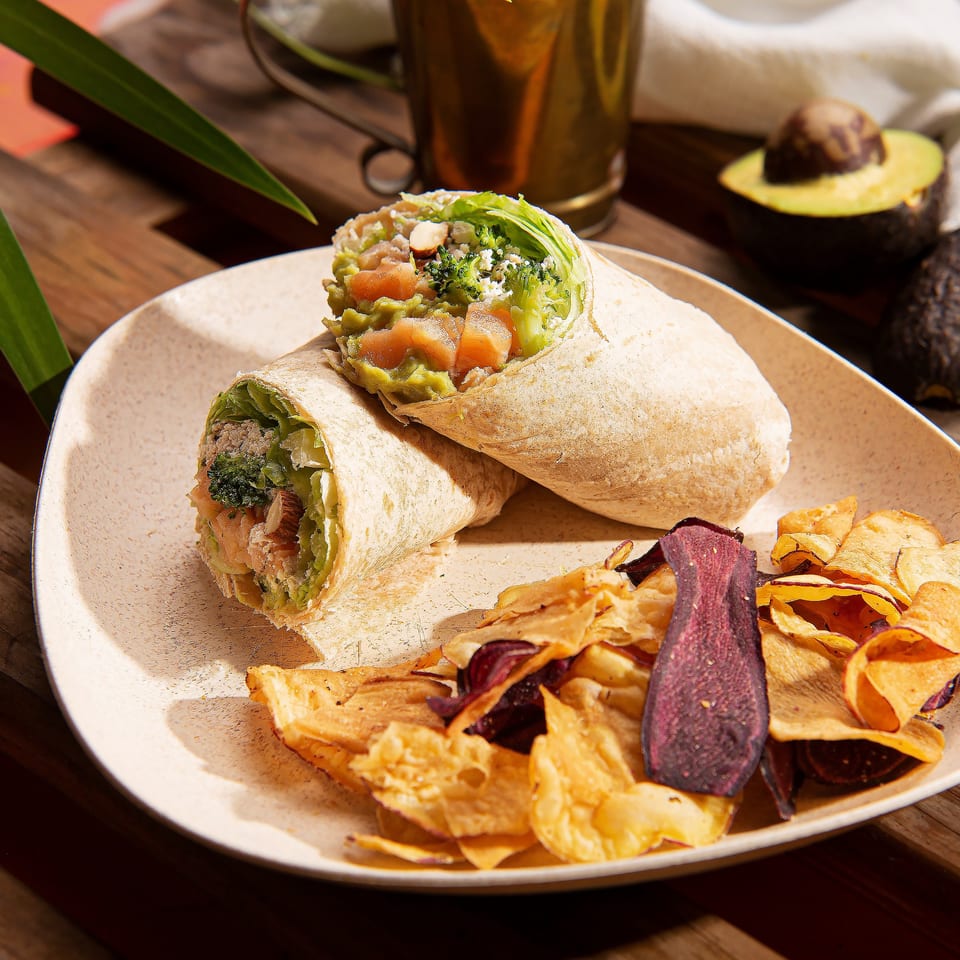 Two Mexican burritos with avocado, broccoli, and salmon, served with root vegetable chips on a plate.
